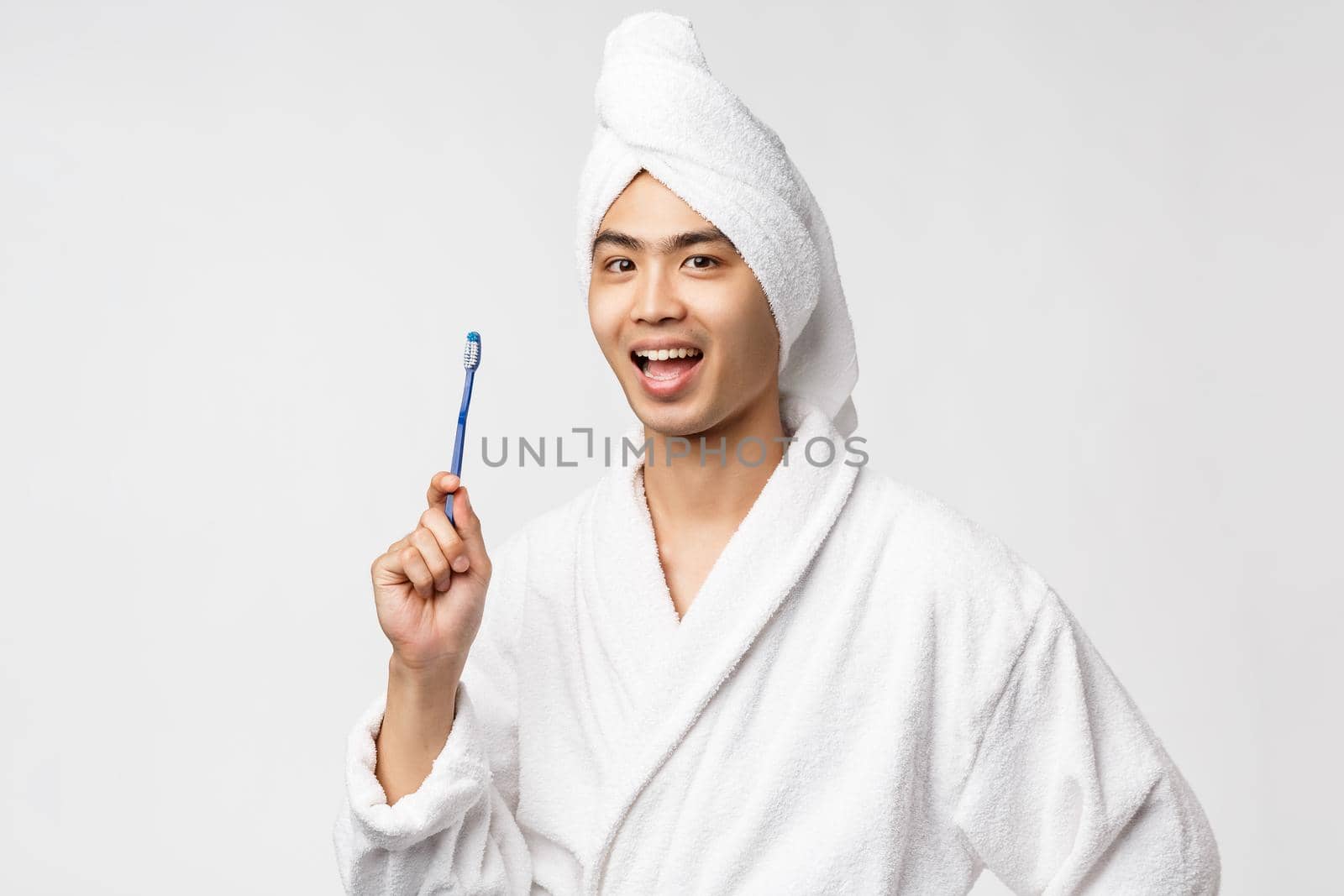 Beauty, spa and leisure concept. Cheerful handsome asian man in bathrobe and bath towel, showing toothbrush and smiling upbeat, washing-up at morning, prepare for big day, white background.