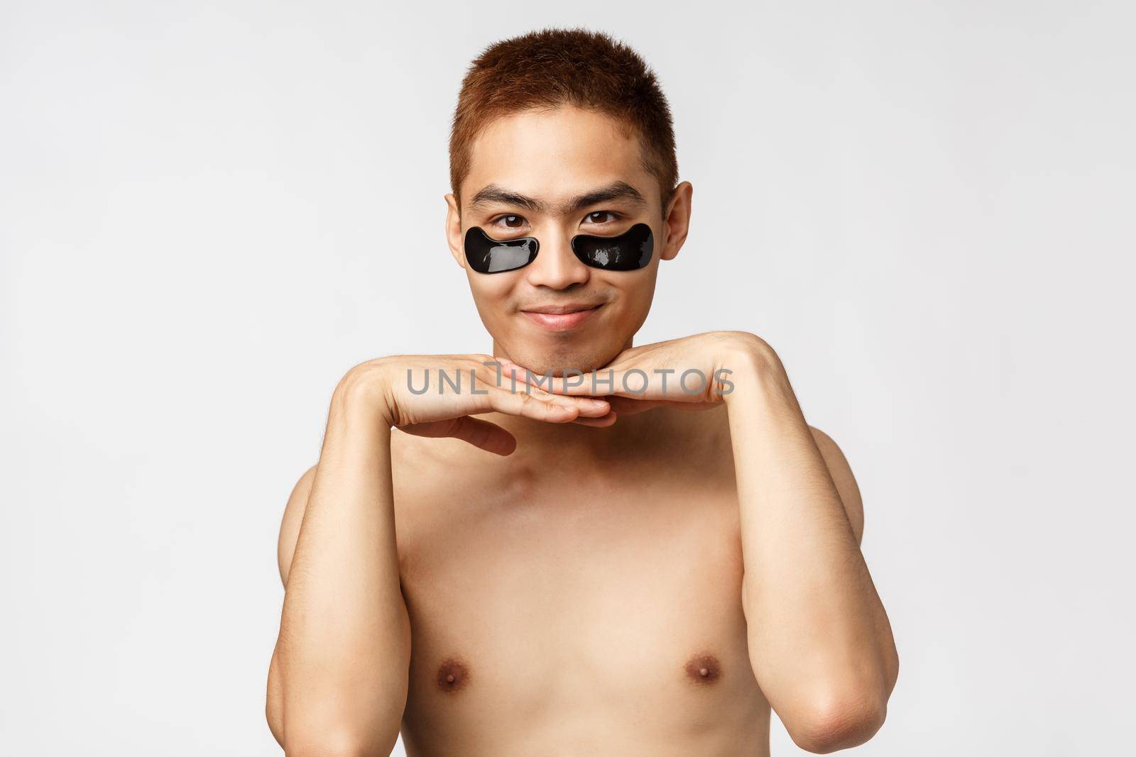 Beauty, people and lifestyle concept. Close-up portrait of sassy and flirty asian naked man wearing black eye-patches, leaning on palms silly smiling, look all lovely, standing white background.