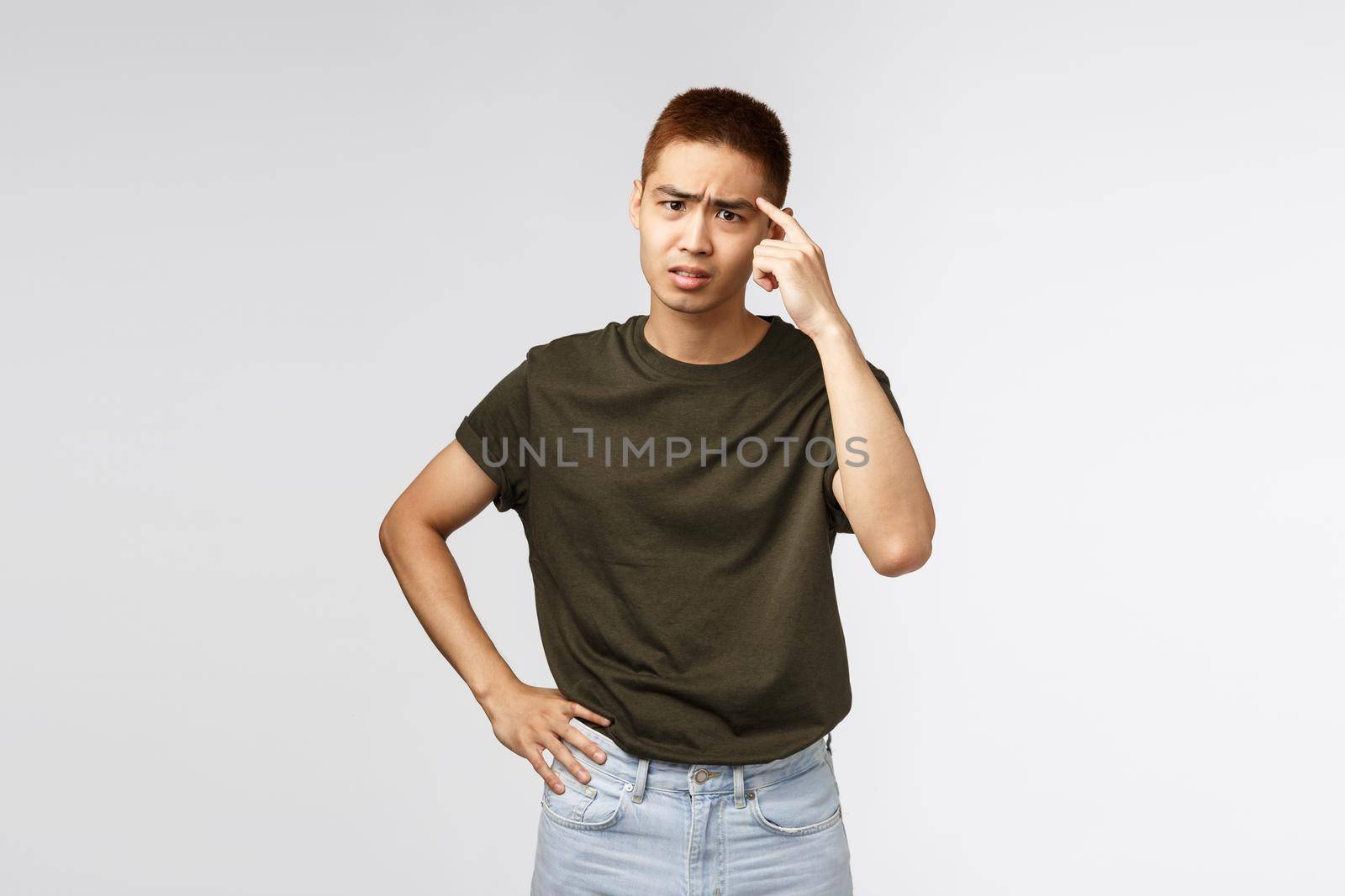 Portrait of annoyed and pissed-off asian man scolding person for being stupid and acting irrational, tap on temple accusing friend being crazy, complaining and frowning displeased, grey background.