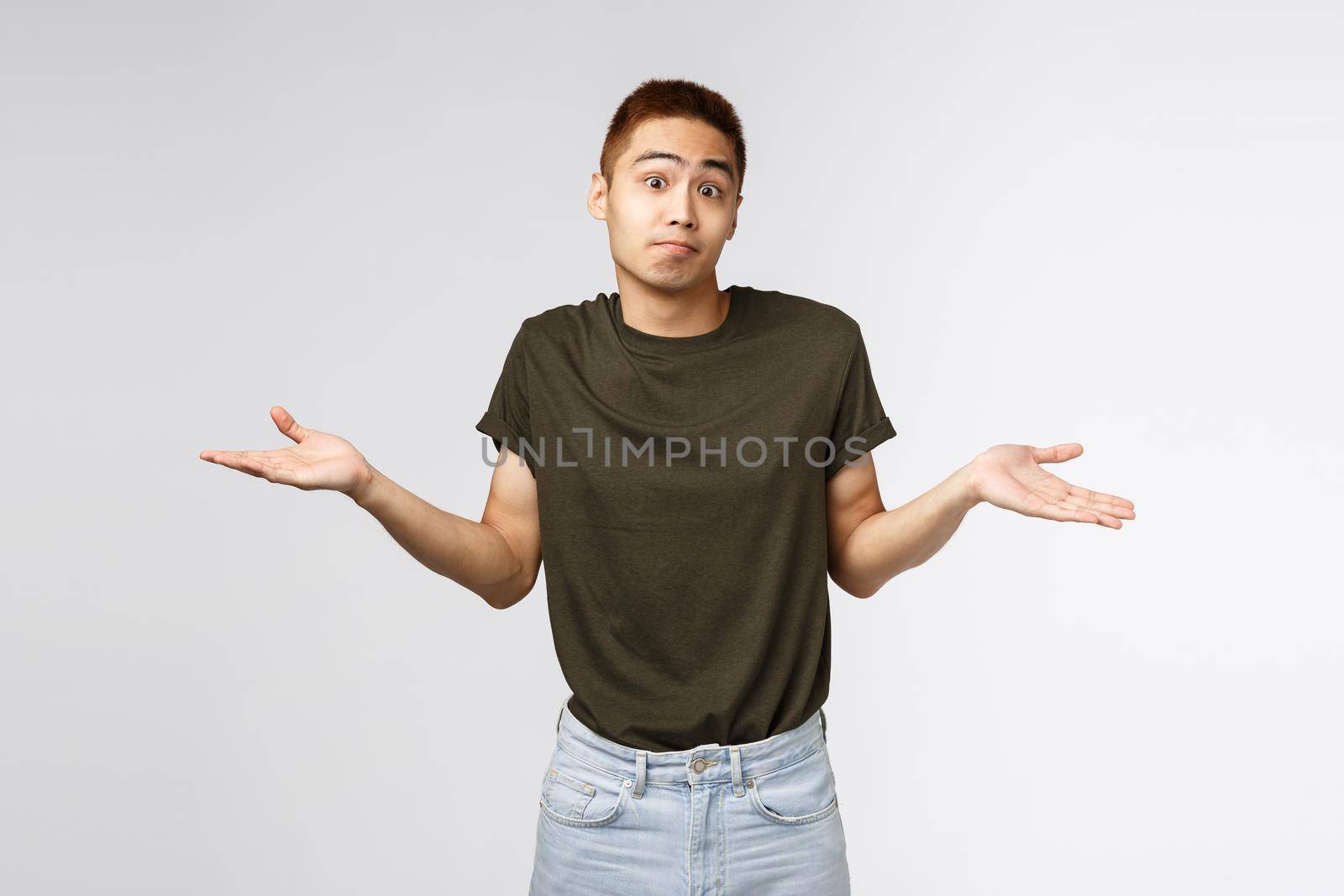 Who knows, I dont aware. Portrait of confused shrugging asian man in greey t-shirt, smirk and apologizing, sorry cant help, standing puzzled and unaware about situation, grey background.
