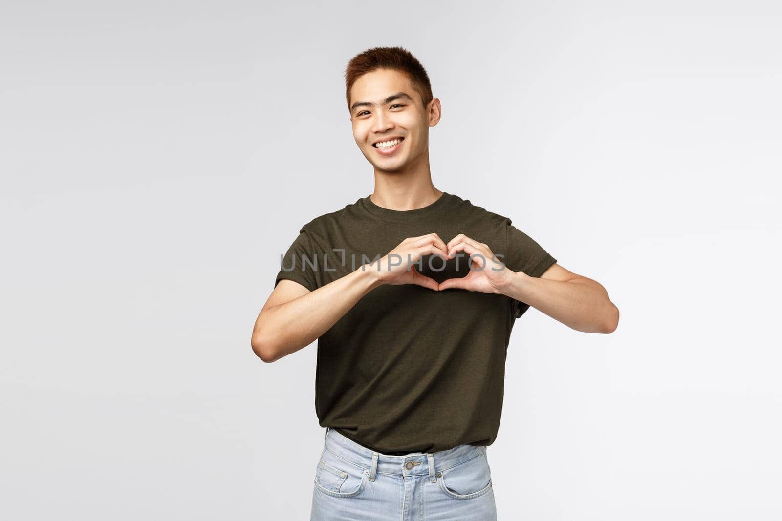 People, emotions and lifestyle concept. Lovely, handsome asian man showing heart over chest and smiling as confess in love, like person, express sympathy, congratulate girlfriend with anniversary.