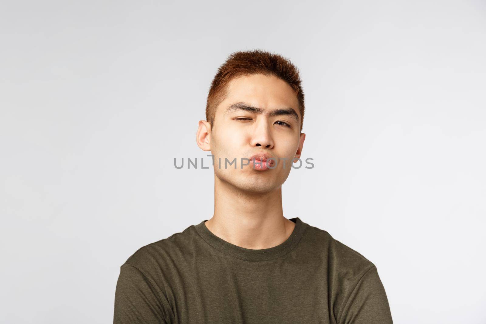 People, different expressions and lifestyle concept. Close-up portrait of funny silly, handsome young guy pouting, folding lips and sending kiss, wink camera, standing romantic over grey background.