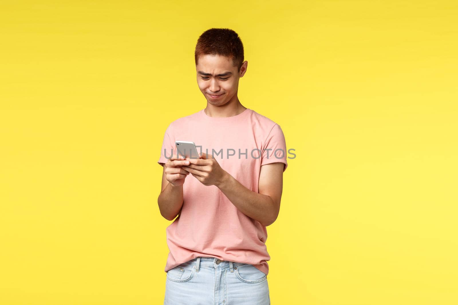 Technology, communication and lifestyle concept. Portrait of touched asian guy looking at adorable picture in his phone, sighing and smiling pleased at display, use mobile phone, texting message.