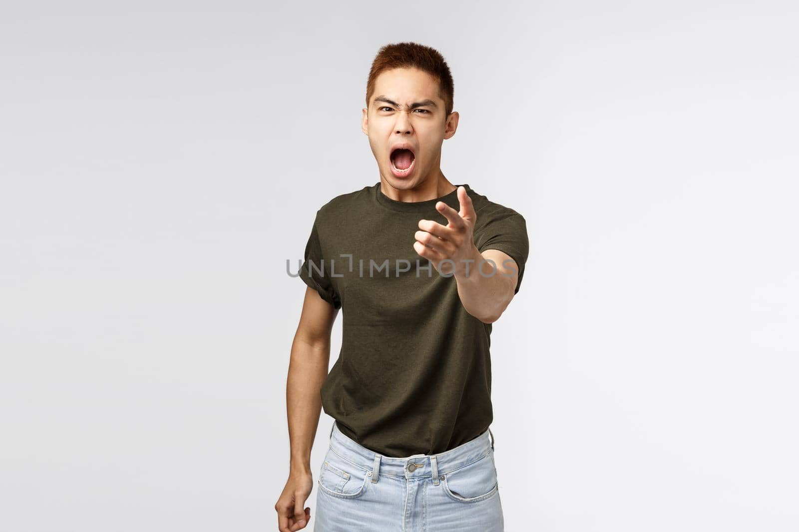 Portrait of angry heartbroken asian boyfriend being cheated on, accuse person for betraying him, pointing fingers and cursing, shouting and blaming someone, grey background.
