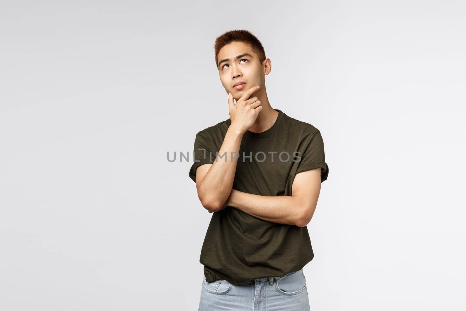Portrait of young asian man thinking and looking up with thoughtful, serious expression, rub chin pondering choice, need make difficult decision, standing puzzled grey background.