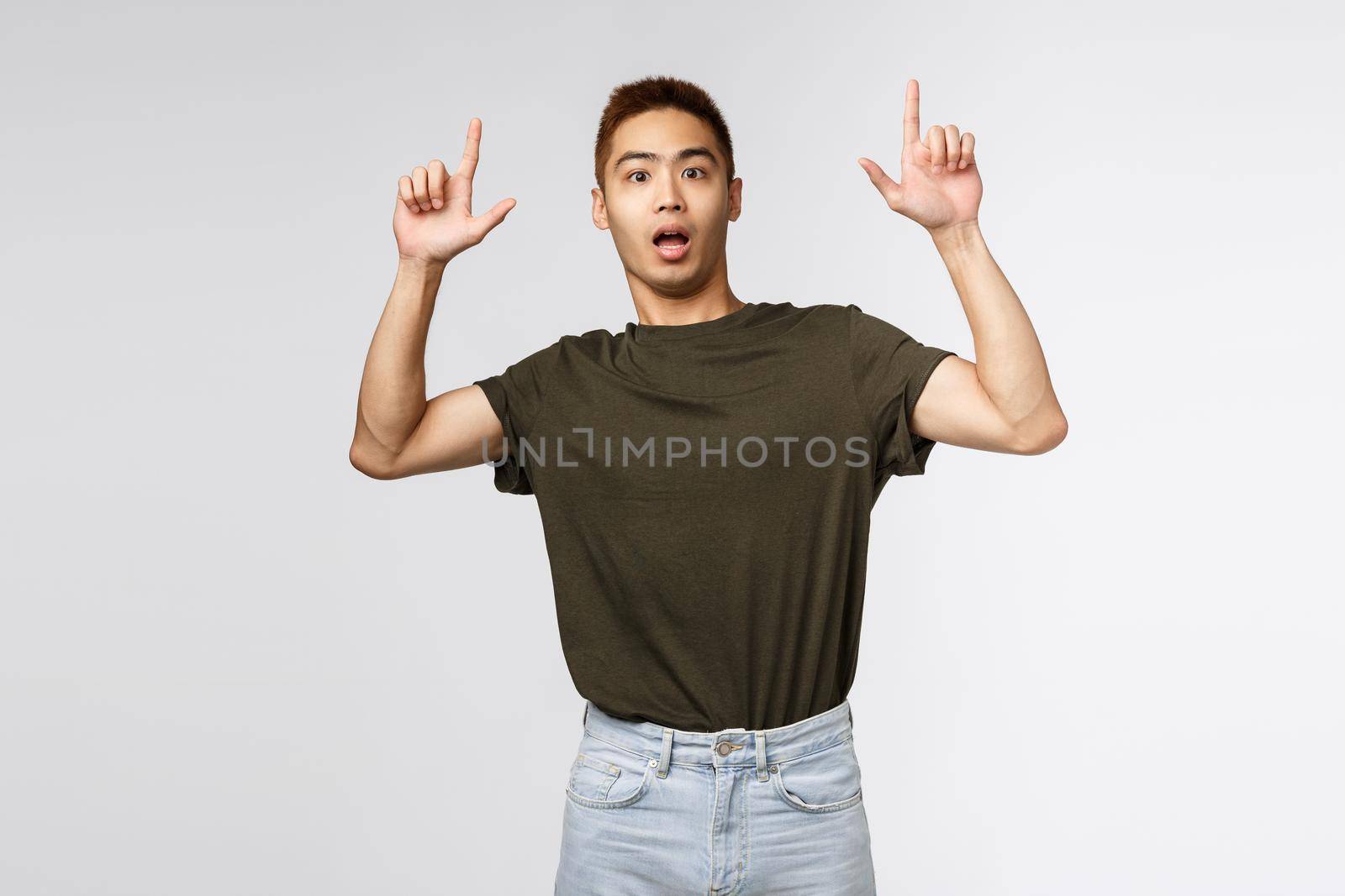 Portrait of shocked and nervous asian man look at camera surprised, pointing fingers up, showing something strange and concerning, asking question about item, grey background by Benzoix