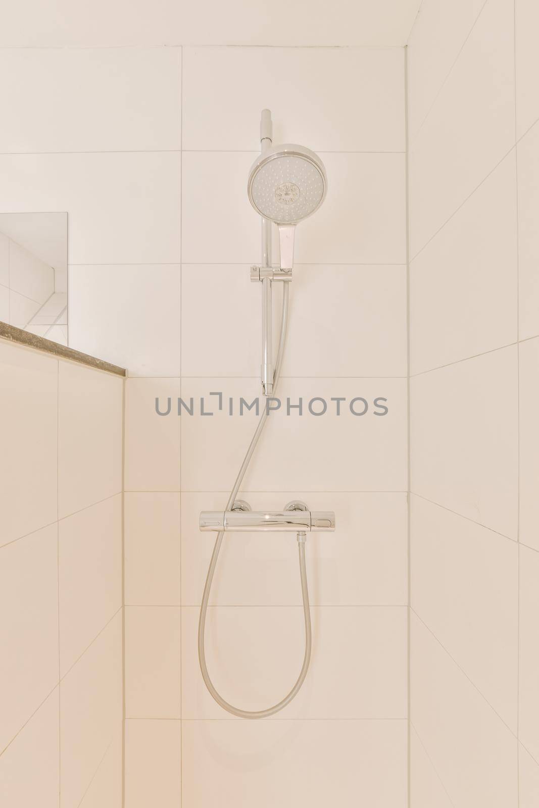 Shower faucets attached to tiled wall near glass partition and ornamental curtail in washroom at home