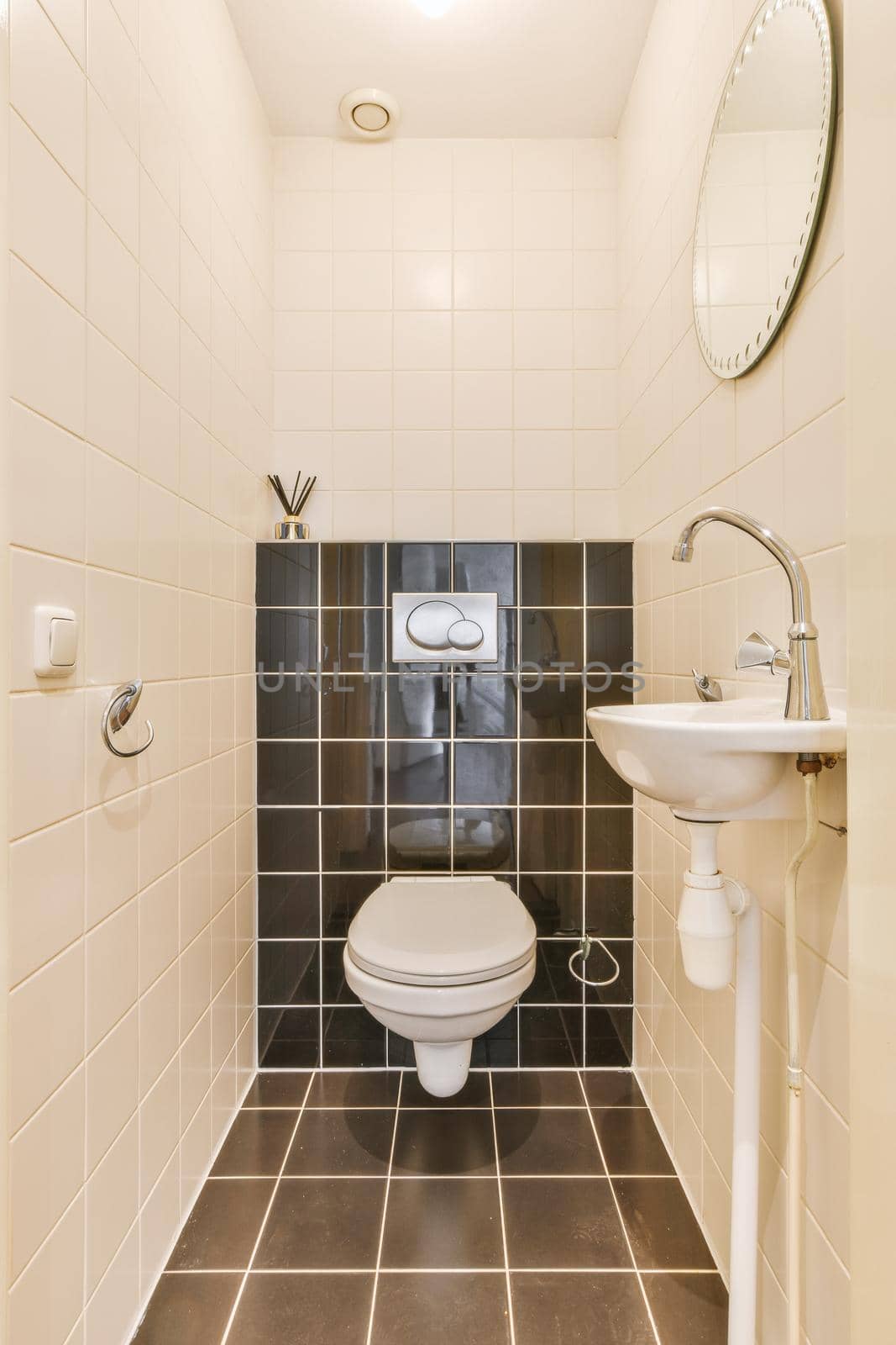 Wall hung toilet and small sink in corner in lavatory room with beige tile