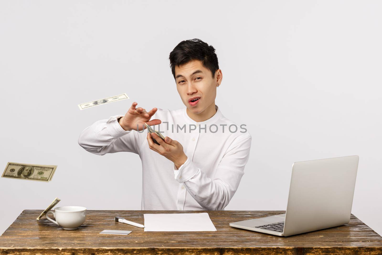 Time to party. Carefree wealthy and successful young chinese male entrepreneur, throwing money at camera with sassy delighted expression, wasting cash, playing with dollars, white background.