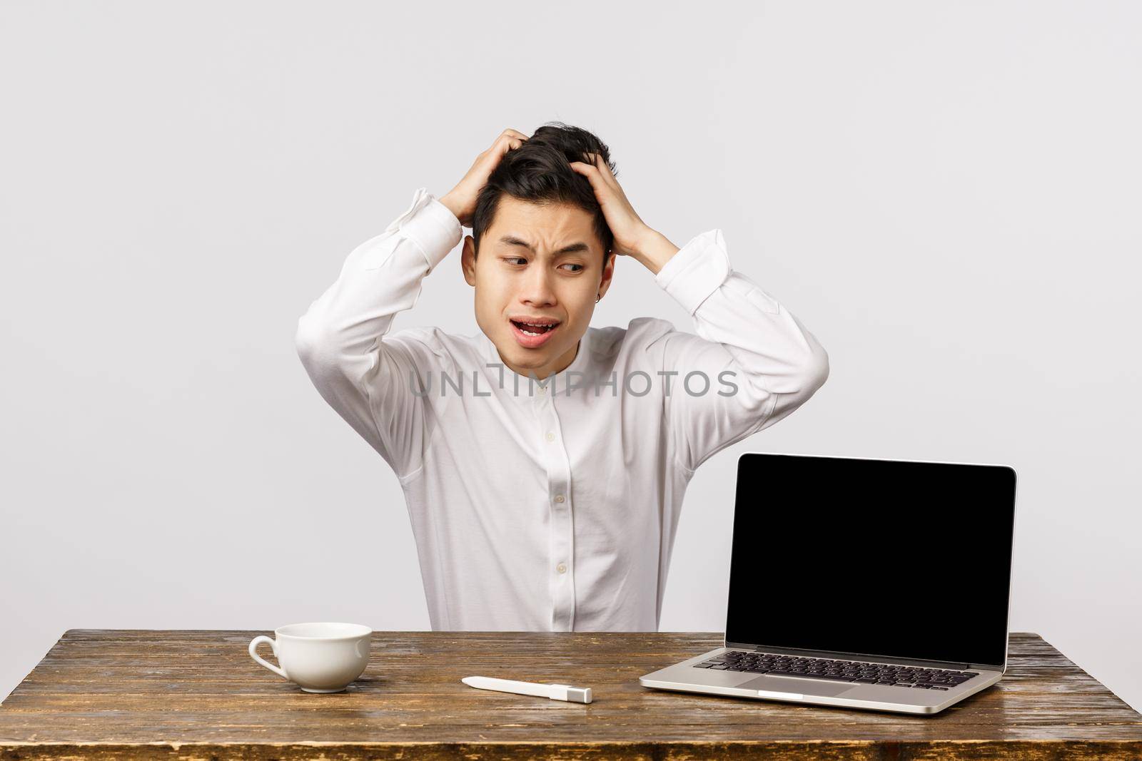 Oh god what have I done. Puzzled and anxious, embarrassed young asian man in shirt, grab head shocked and distressed, staring laptop display, react to embarrassing video posted online.