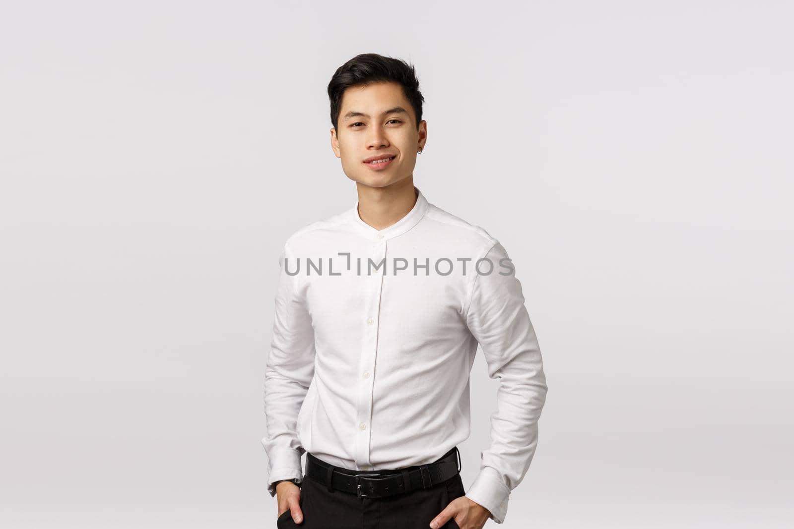 Business, success and wellbeing concept. Handsome young asian businessman working with finances, have lucky dat, hold hands in pockets, smiling self-assured, standing white background.