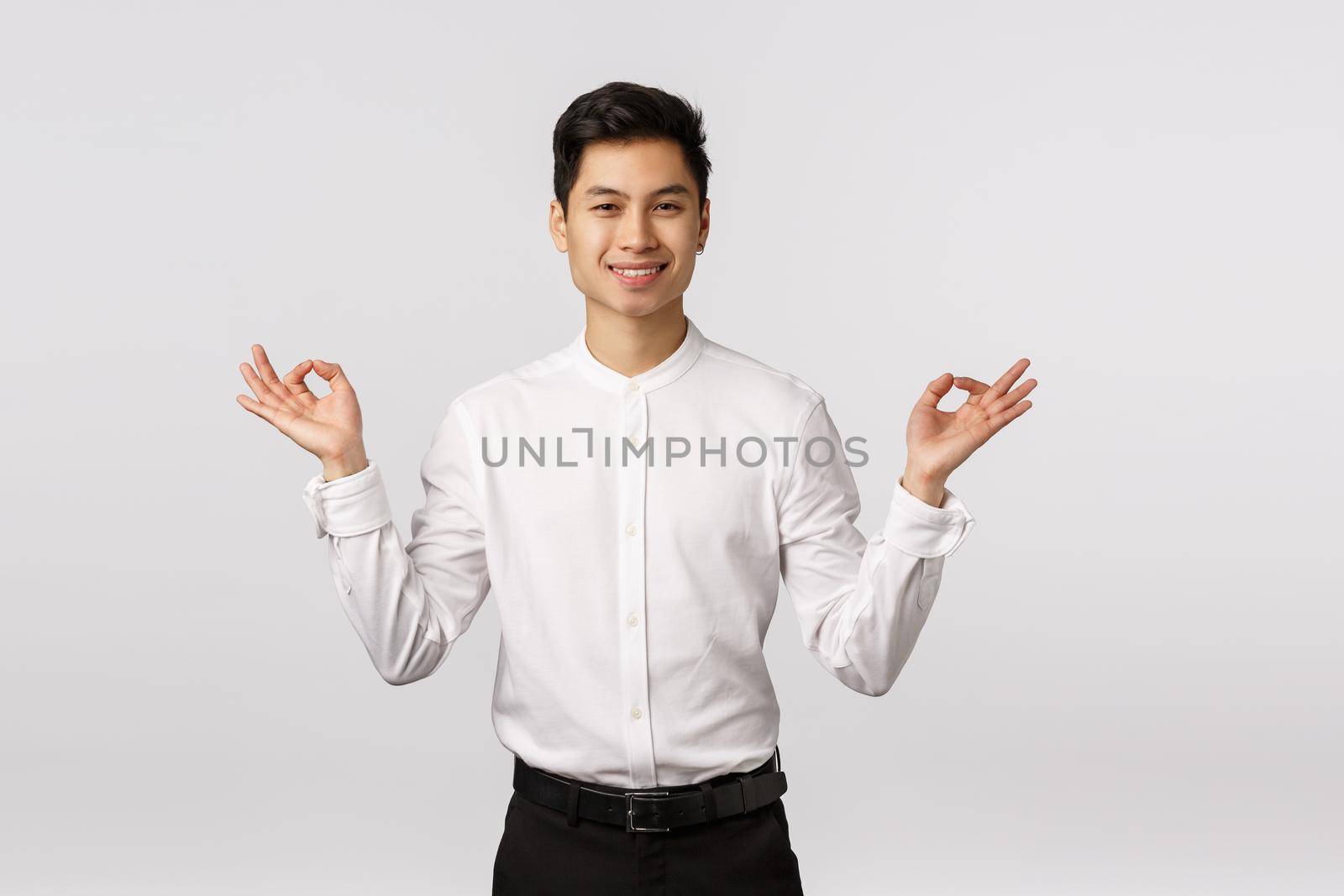 Peaceful and carefree, smiling relaxed cute asian businessman in white shirt, pants, formal outfit, trying take rest from business worries, meditating smiling glad, hold hands sideways, reach nirvana.