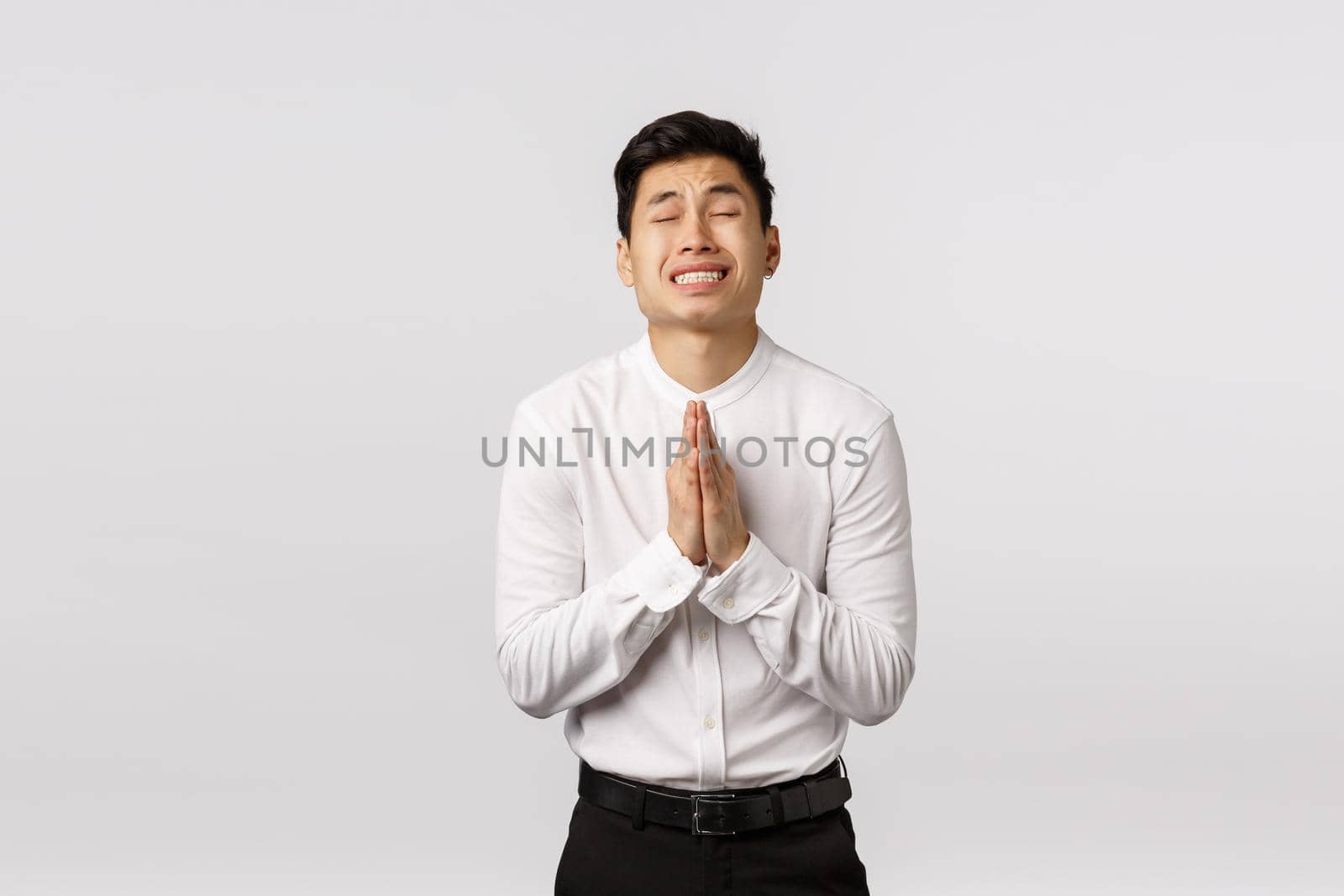 Worried, hopeful young asian male entrepreneur, businessman praying, begging boss give him second chance, close eyes clench teeth nervously supplicating, standing white background.