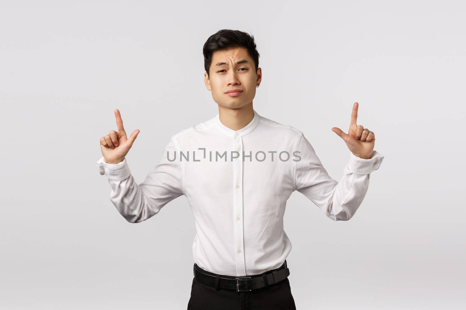 Skeptical attractive asian businessman have doubts, pointing up frowning with disbelief or hesitation, smirk judgemental and disdain, dont believe this product worth his attention, white background.