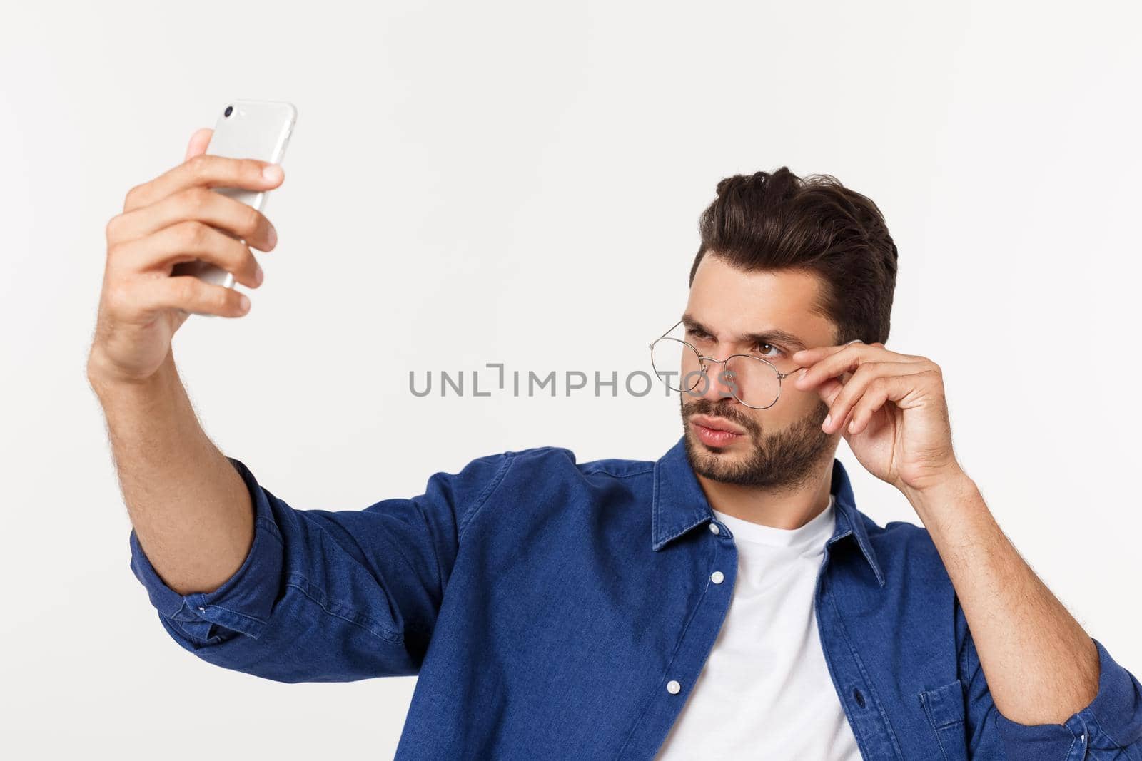 Portrait of an attractive young man taking a selfie while standing and pointing finger isolated over white background