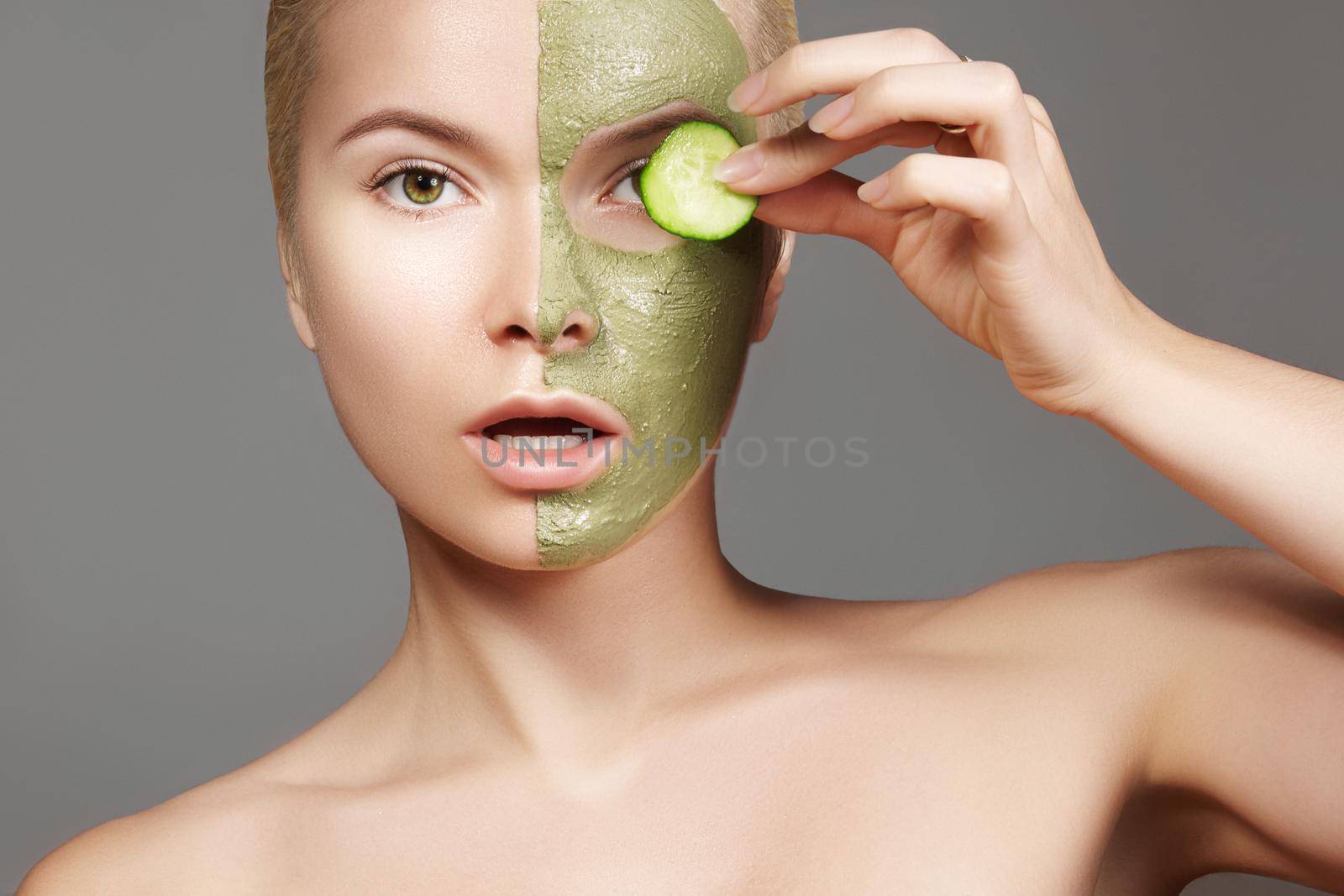 Beautiful Woman Applying Green Facial Mask. Beauty Treatments. Close-up Portrait of Spa Girl Apply Clay Facial mask and Cucumber on grey background