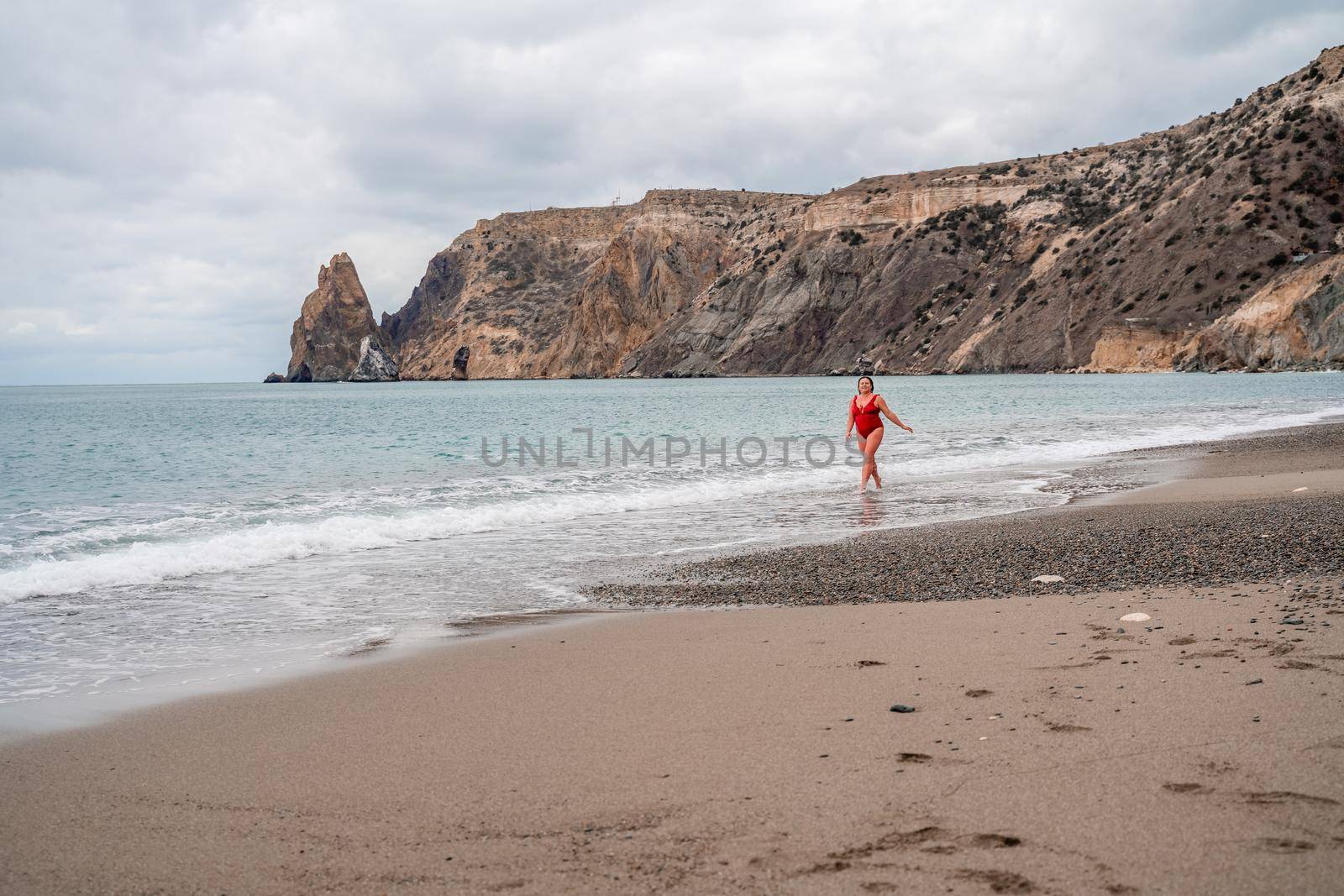 Woman in a bathing suit at the sea. A fat young woman in a red swimsuit enters the water during the surf.