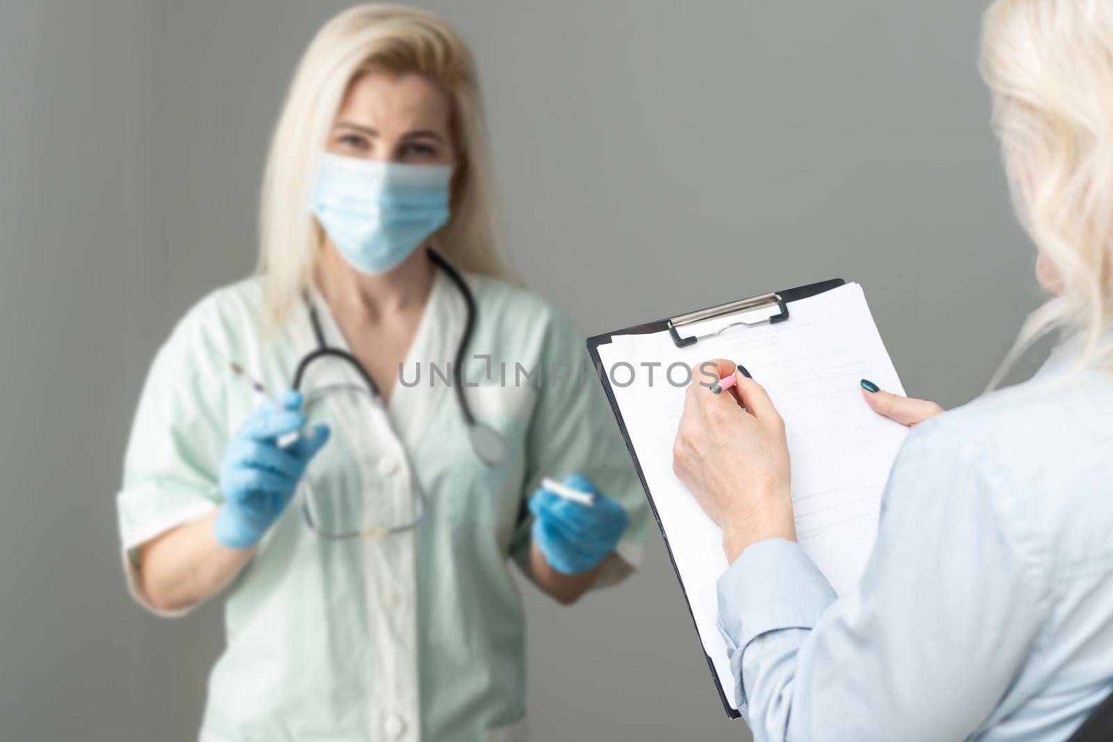 Middle aged female doctor therapist in medical mask on consultation with patient in office.