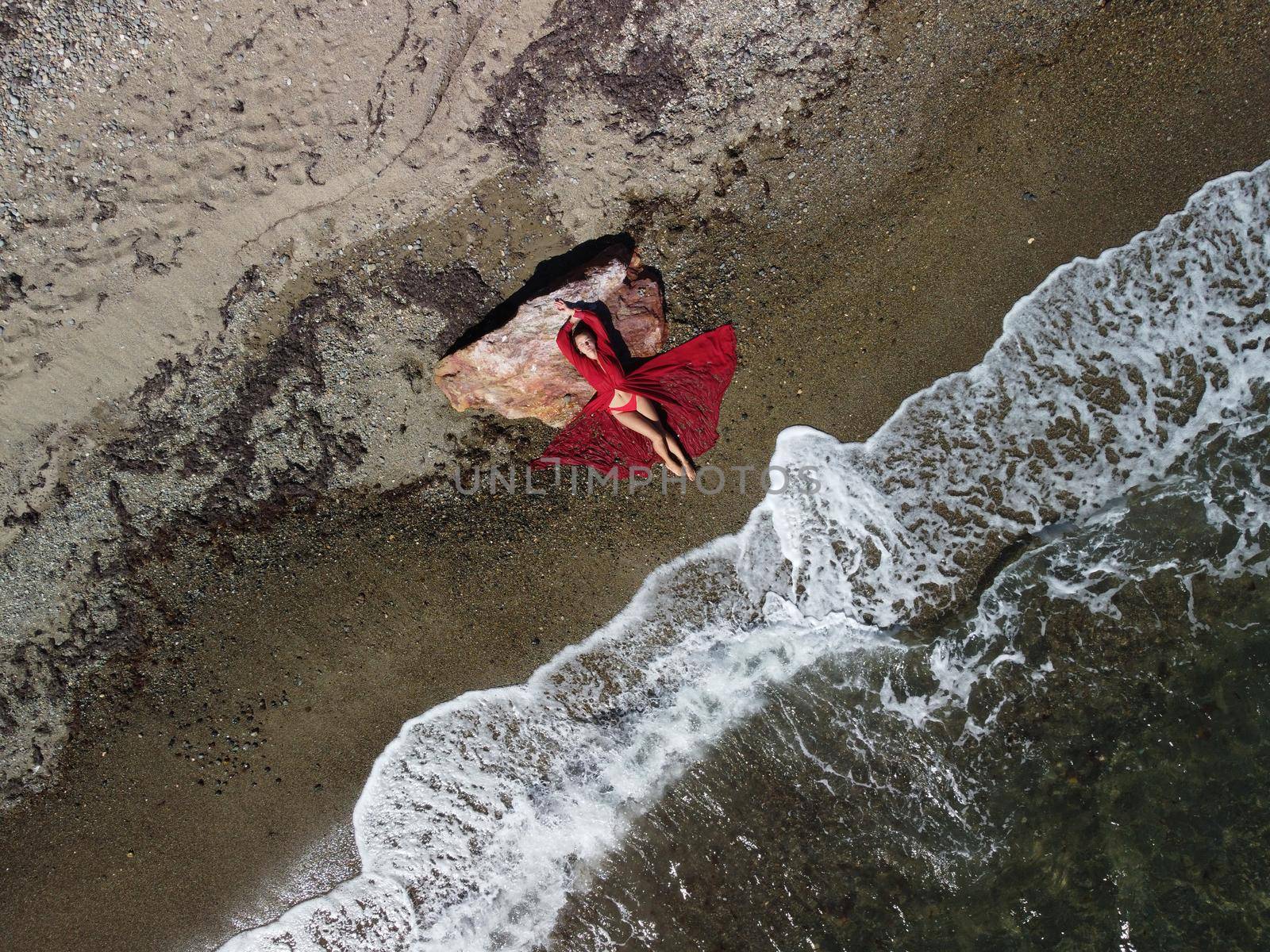 Young sensual blonde woman sitting on the rock near water at sea and enjoys the sea waves on background of two volcanic rocks, like in Iceland. Dreams holidays and weekend vacation in summer time