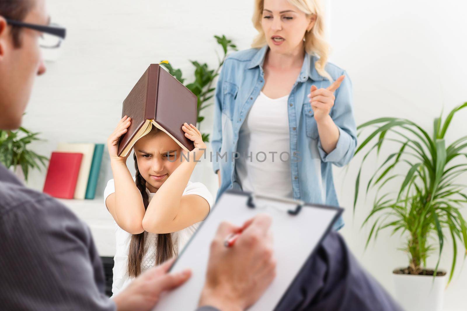 Hand of a professional family psychotherapist writing notes in front of a family with a child during a consultation by Andelov13