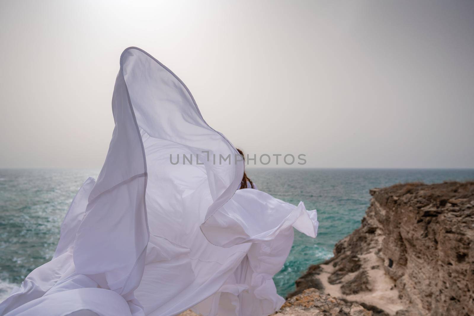 Happy freedom woman on the beach enjoying and posing in white dress. Rear view of a girl in a fluttering white dress in the wind. Holidays, holidays at sea. by Matiunina