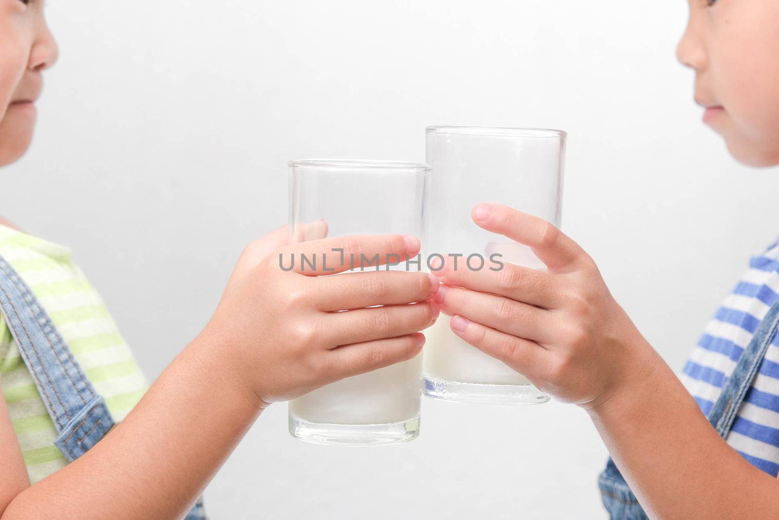 Two little sisters drinking tasty milk from glasses isolated on white background. Happy 6- and 5-year-old sisters drink healthy milk before school. by TEERASAK