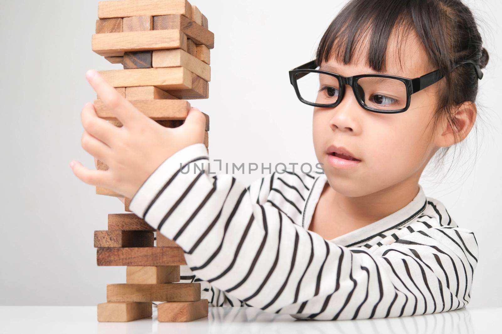 Asian children playing wooden blocks on table at home. Cute little girl having fun playing with building blocks. Wooden block tower building game. Toys for the development of children by TEERASAK