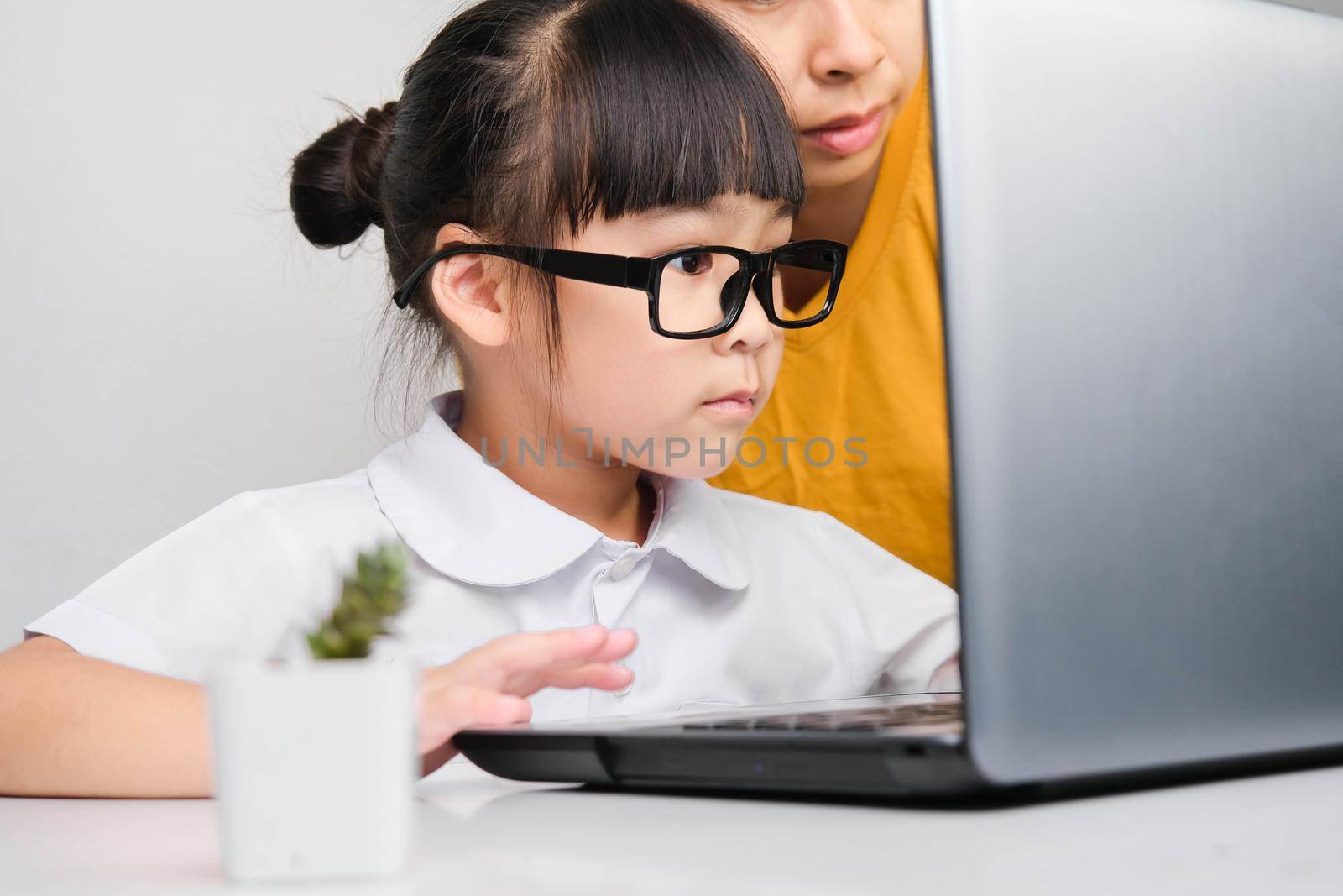 Mother teaches her daughter the basics of business. Little businesswoman with laptop working in office with mother. Children and business concepts by TEERASAK
