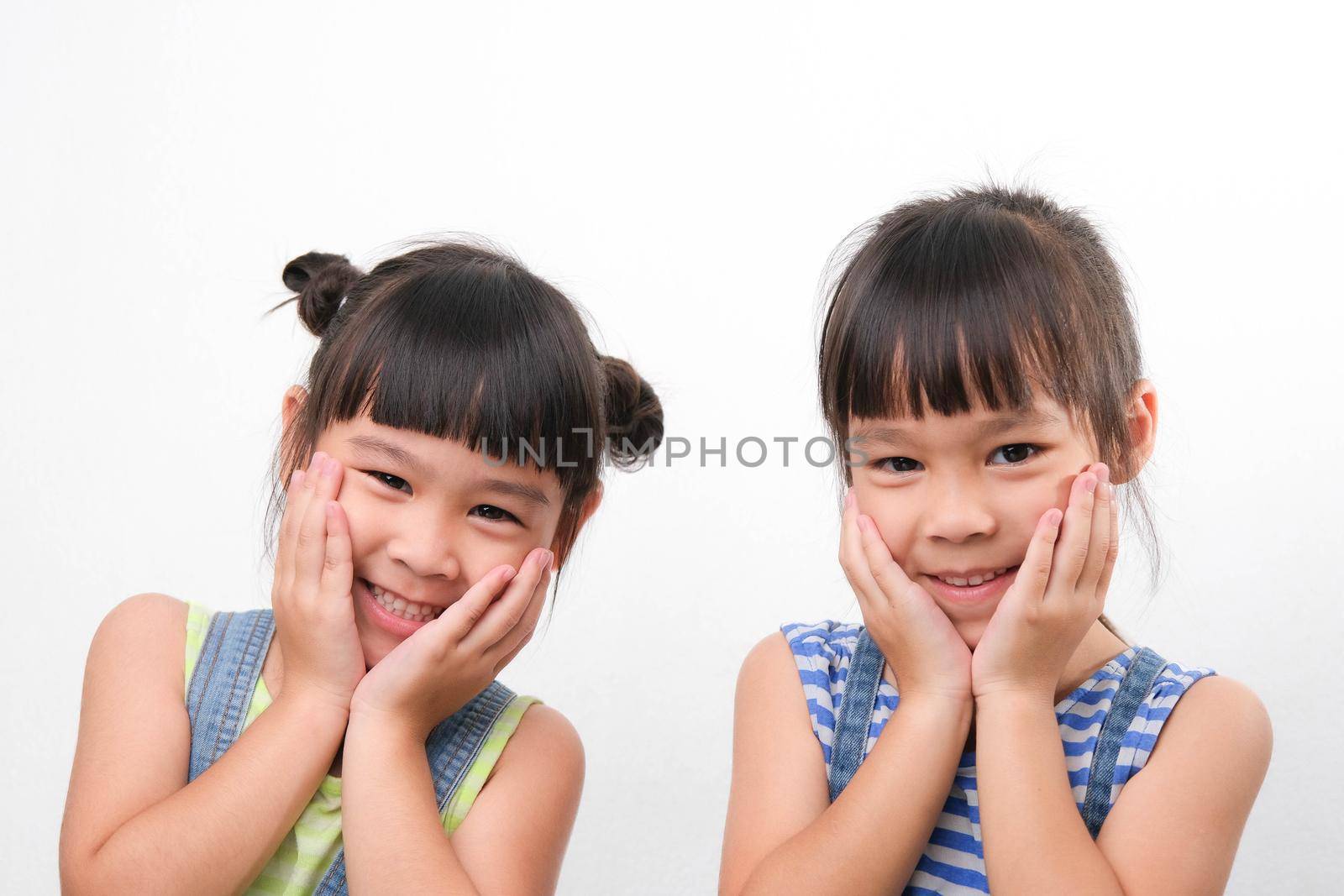 Two little sisters gesturing to look attractive, cute, healthy, cheerful looking at the camera, isolated on white background. friendship and love concept. by TEERASAK