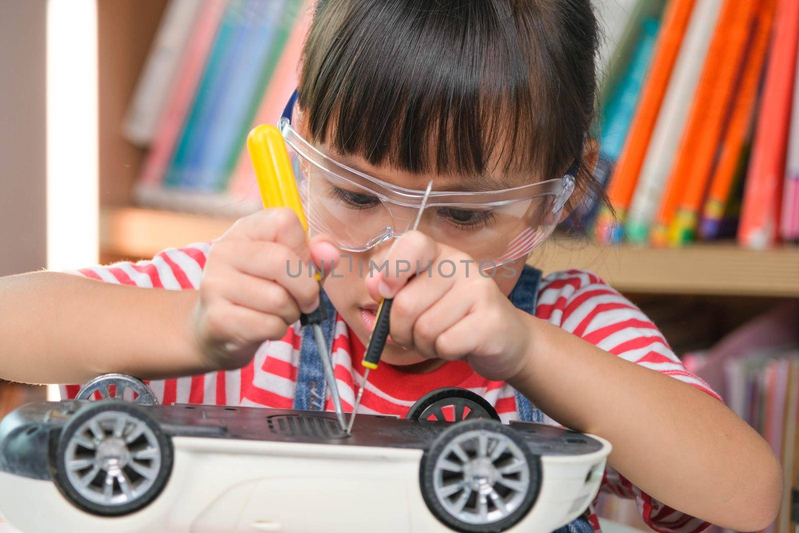 Concentrated little girl repairing her toy car with a tool in hand and carefully assembles toy car with screwdriver. STEM Hobbies for advanced smart kids. by TEERASAK