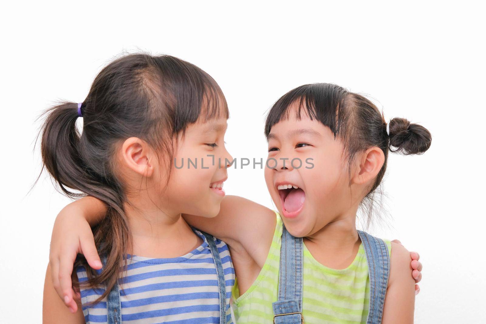Two little sisters hugging and looking at each other isolated on white background. Two pretty little girls sisters happily cuddle and laugh. friendship and love concept. by TEERASAK