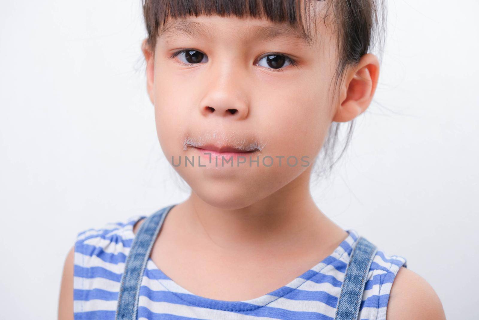 Cute little girl holding a glass of milk and licking her lips on white background. Small girl at home with smiling face, feeling happy enjoying drinking milk and looking at camera.