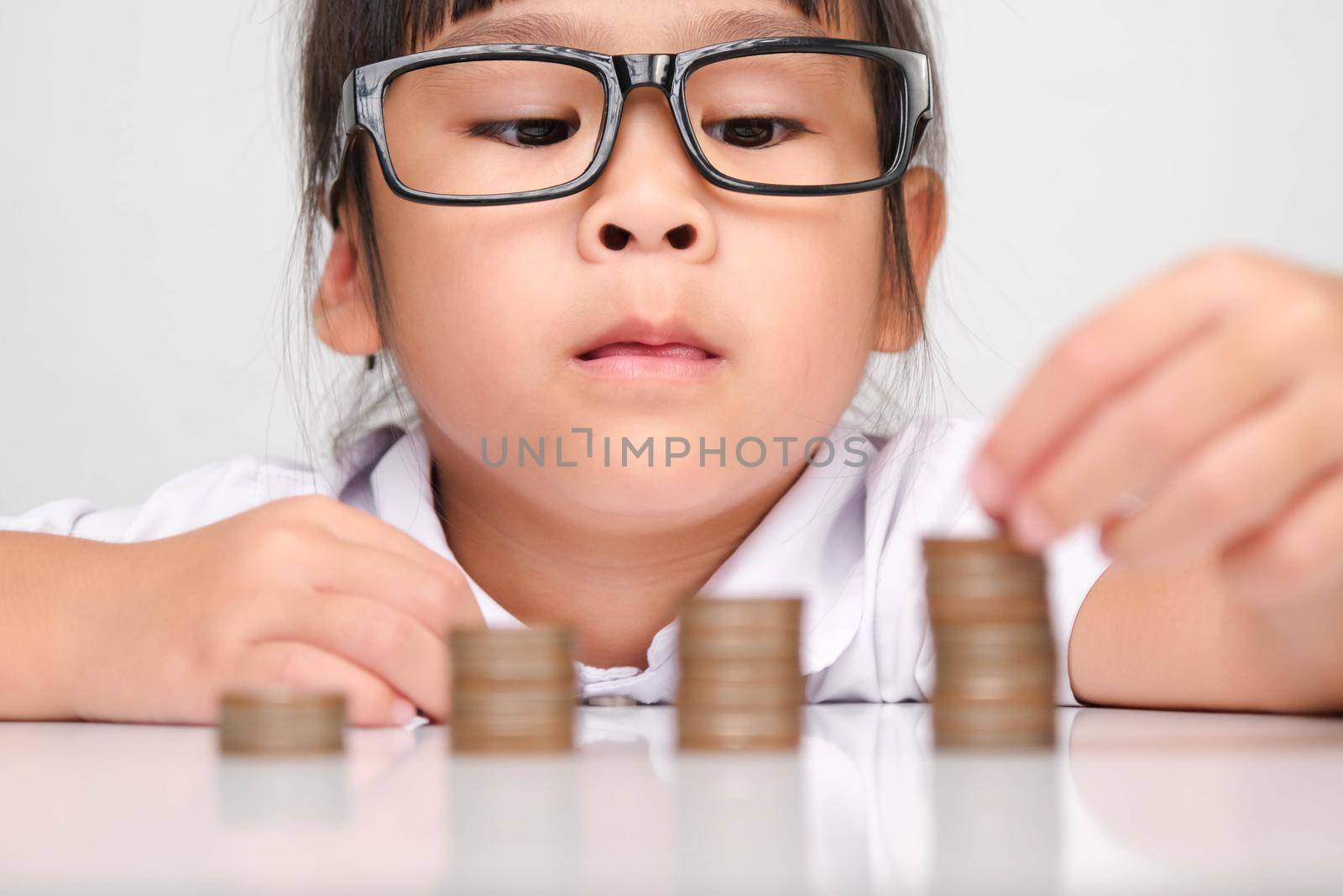 Cute asian little girl making stacks of coins. Little kids save money for future education. by TEERASAK