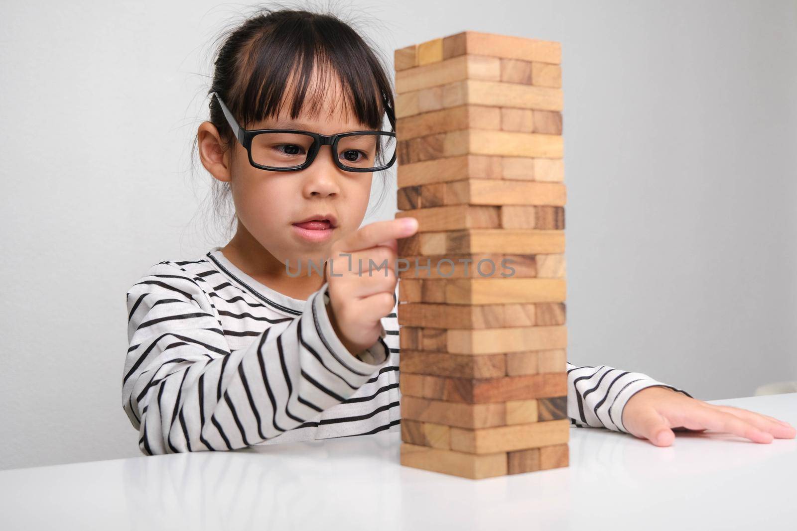 Asian children playing wooden blocks on table at home. Cute little girl having fun playing with building blocks. Wooden block tower building game. Toys for the development of children