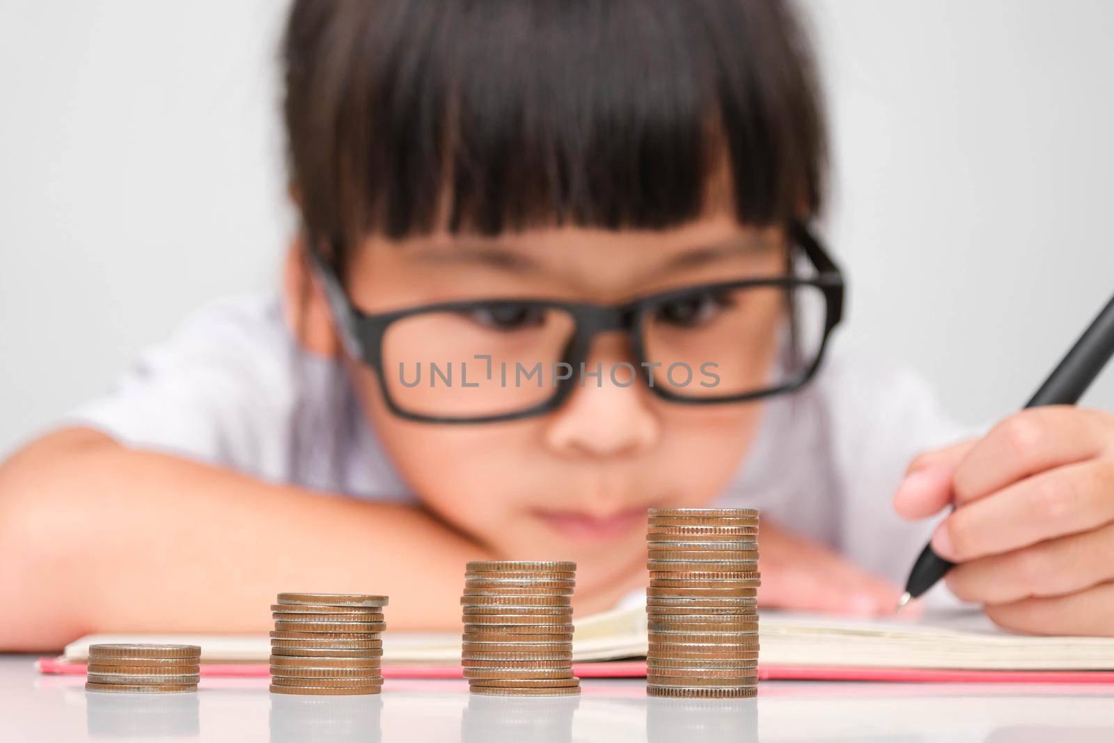 Cute Asian little girl making stacks of coins and taking notes. Little kids save money for future education.