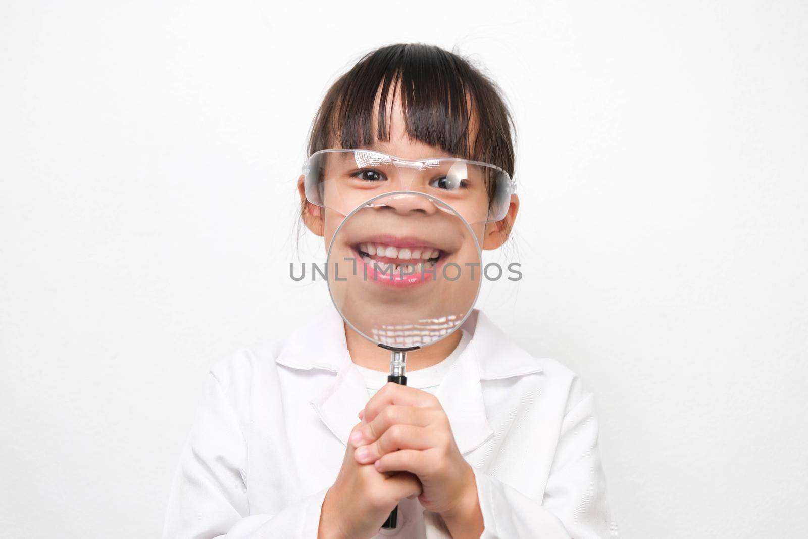 Portrait of a smiling little scientist holding a magnifying glass on a white background. A little girl role playing in a doctor or science costume.
