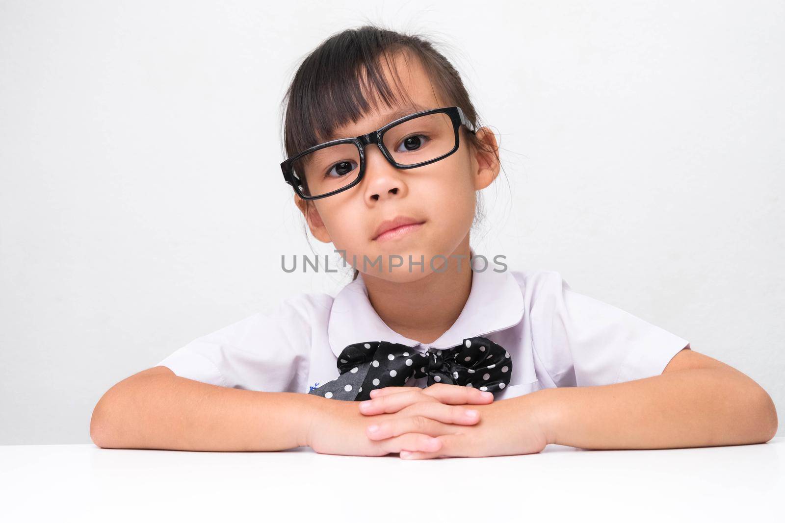 Cute Asian little girl playing teacher role game or a small businesswoman sitting on table in the office and looking at the camera. Homeschool children's play and learning. by TEERASAK