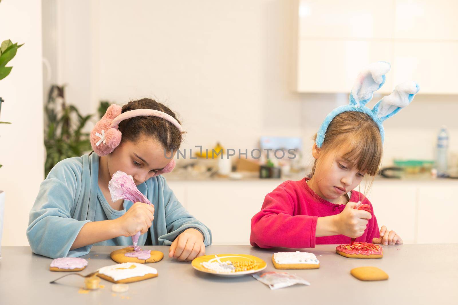 two little sisters decorating homemade cookies in the kitchen at home