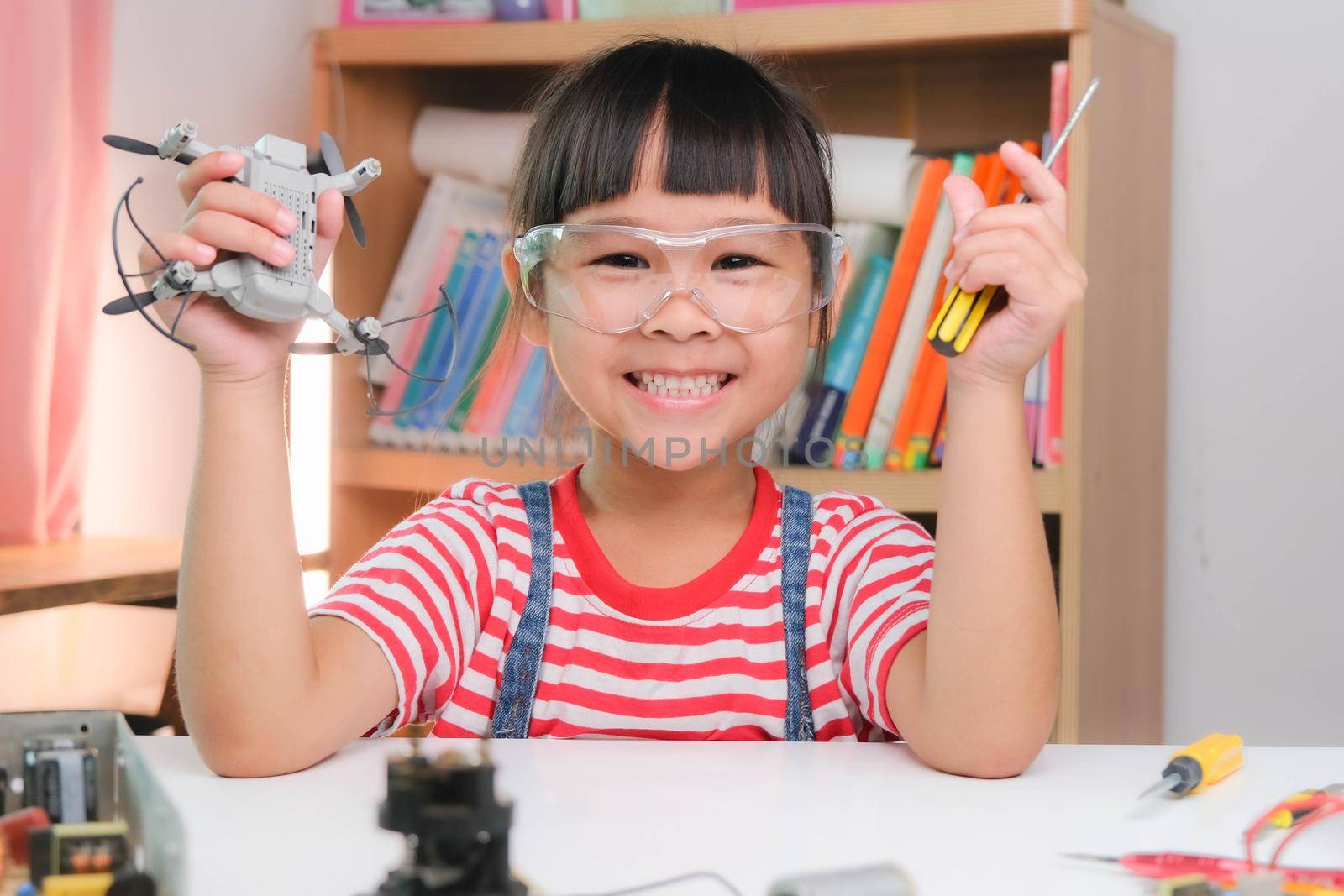 Concentrated little girl repairing her toy drone with a tool in hand and carefully assembles toy drone with screwdriver. STEM Hobbies for advanced smart kids.