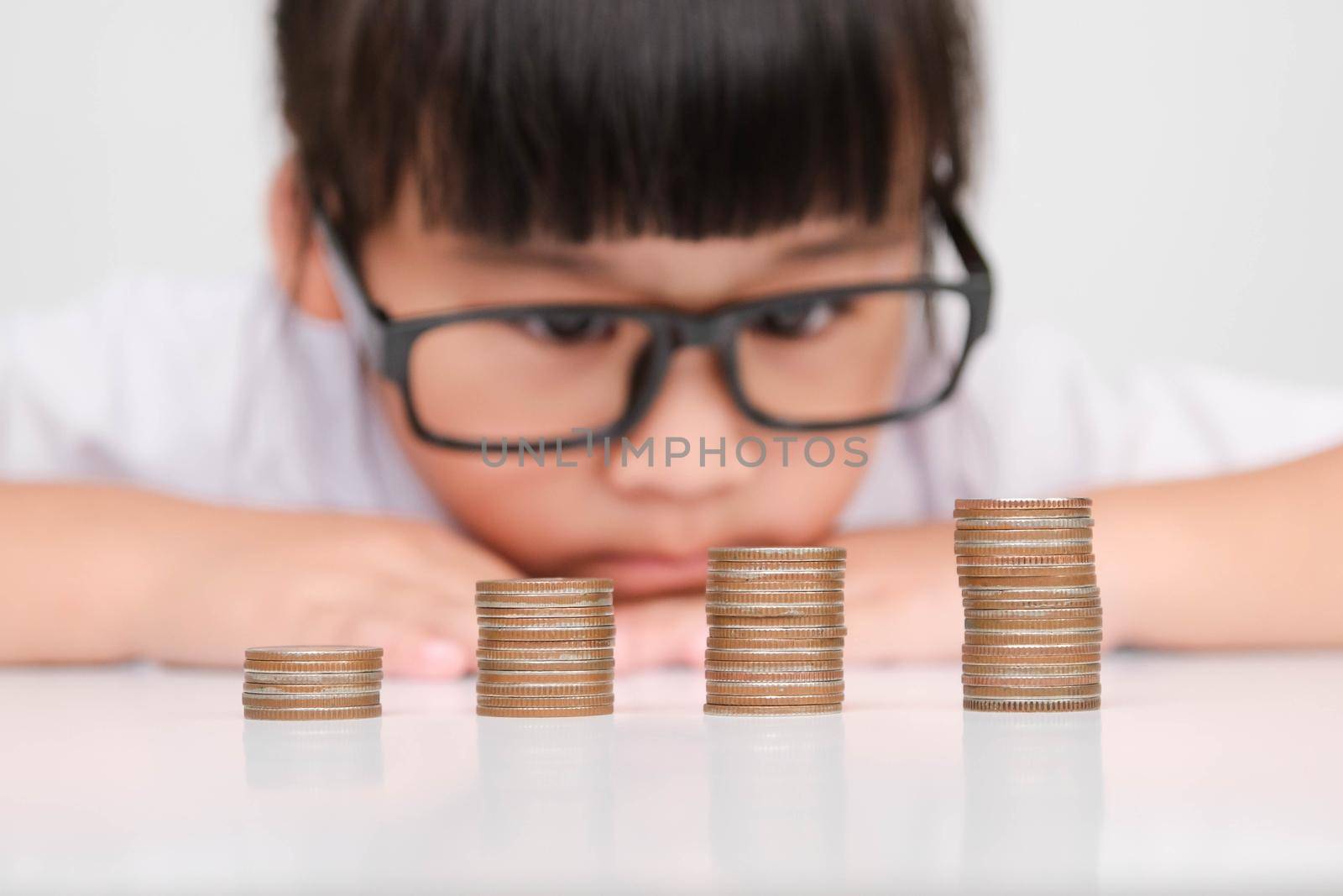 Cute asian little girl making stacks of coins. Little kids save money for future education. by TEERASAK