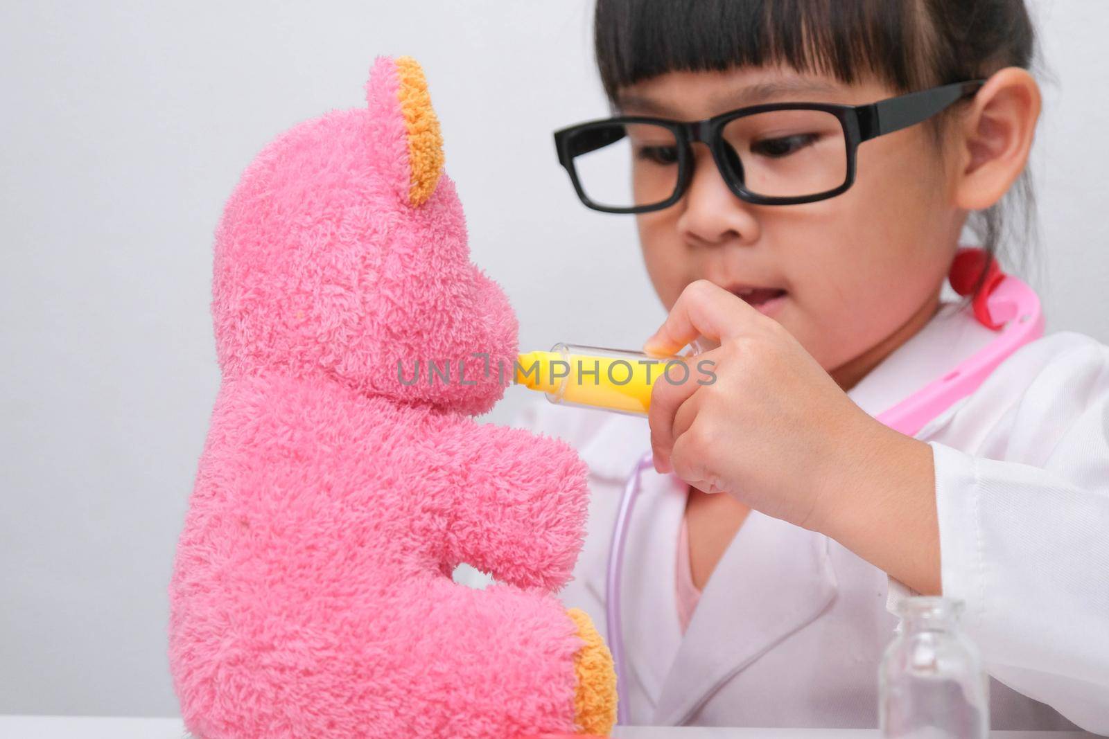 Cute Asian little girl playing doctor role game is giving injection to her sick teddy bear friend. Homeschool children's play and learning.