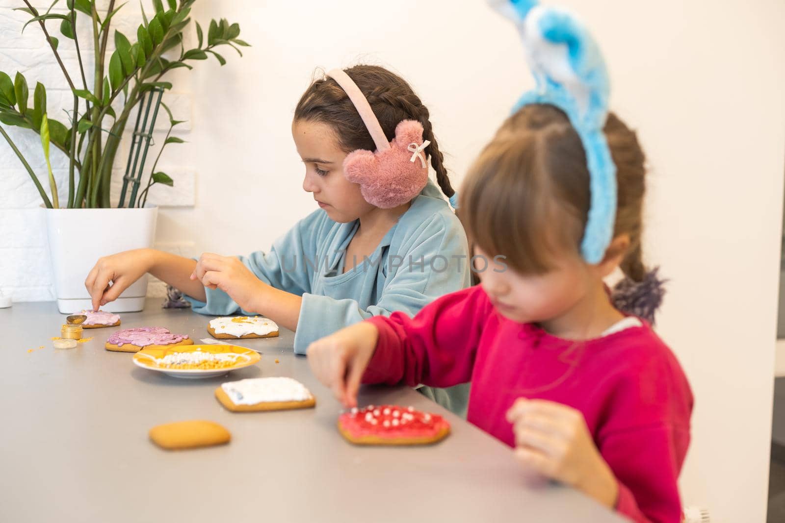 two beautiful sisters decorate and eat delicious cakes at a wooden table.