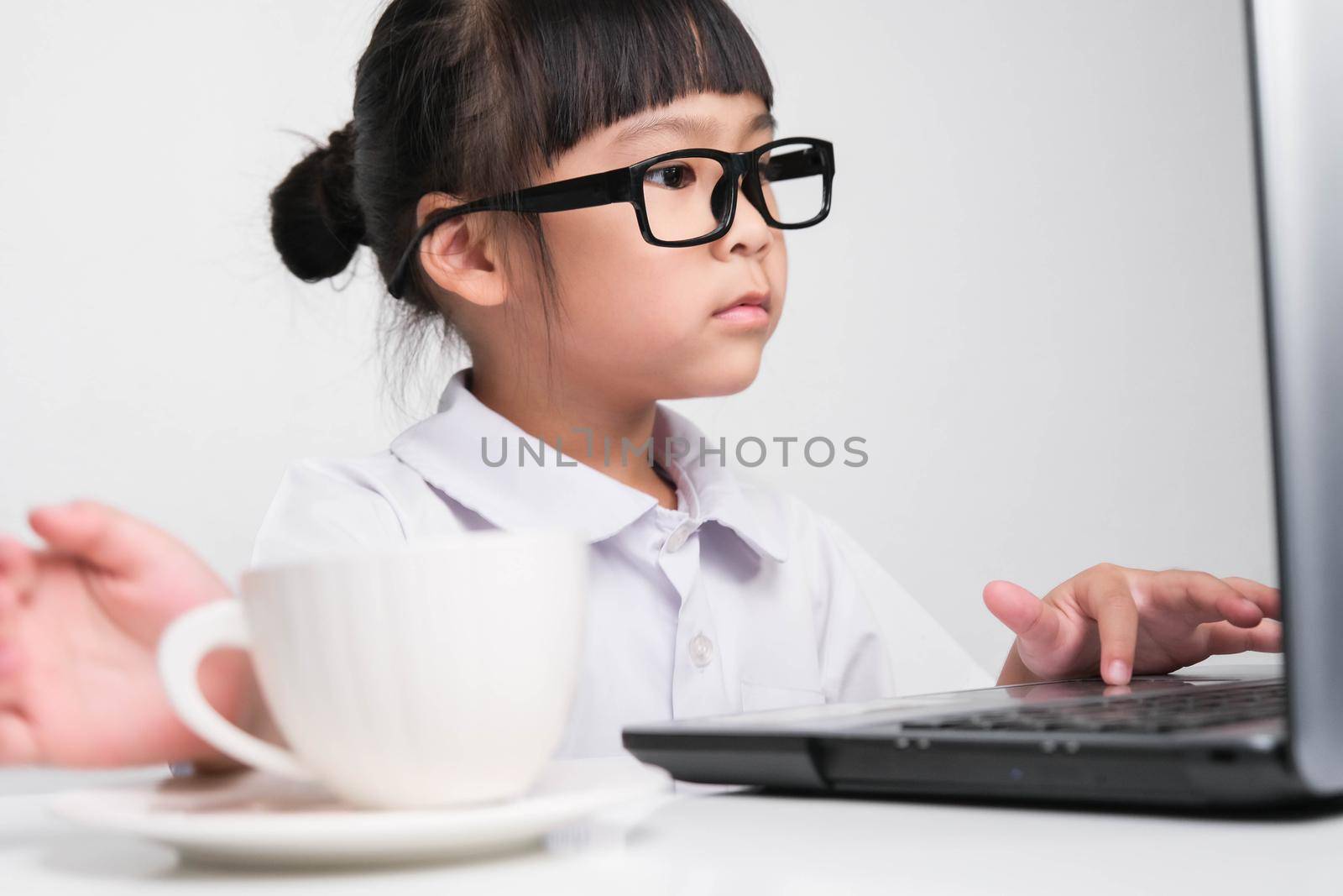 Little businesswoman with laptop working in office with coffee cup on table. children and business concept. by TEERASAK