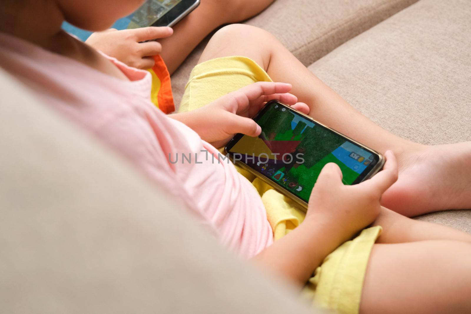 Two little girls addicted to mobile phones. Asian sisters are playing games or watching cartoons with their smartphones on the sofa at home.