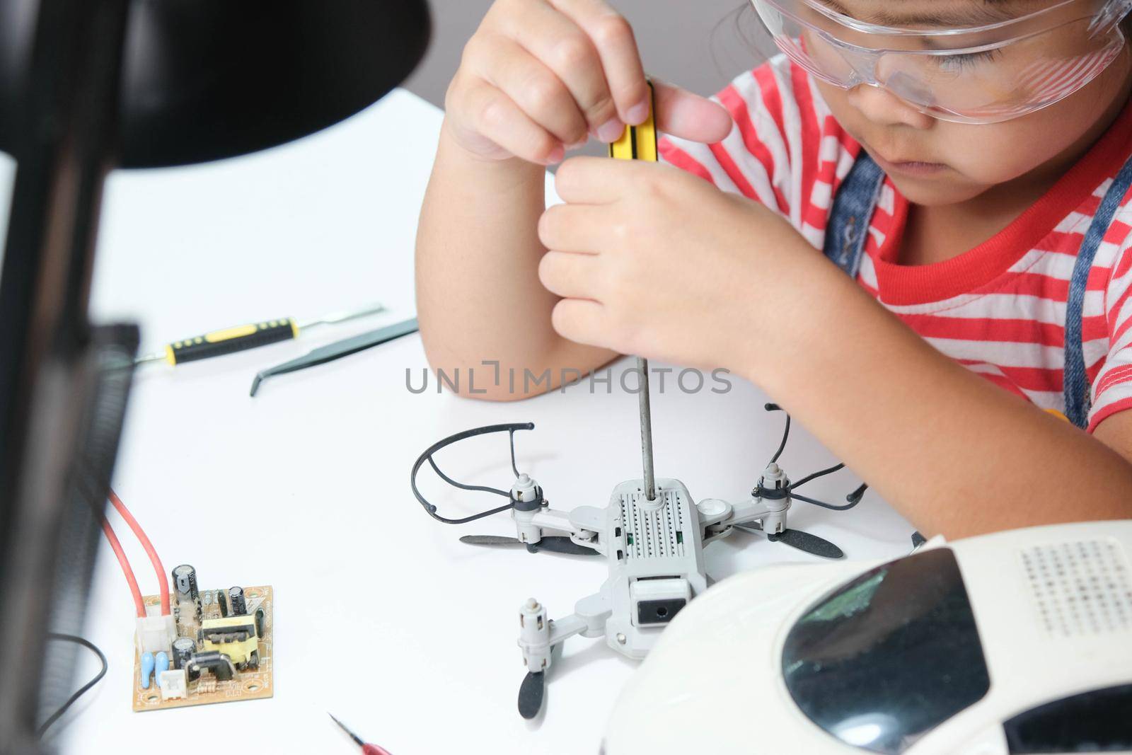 Concentrated little girl repairing her toy drone with a tool in hand and carefully assembles toy drone with screwdriver. STEM Hobbies for advanced smart kids. by TEERASAK