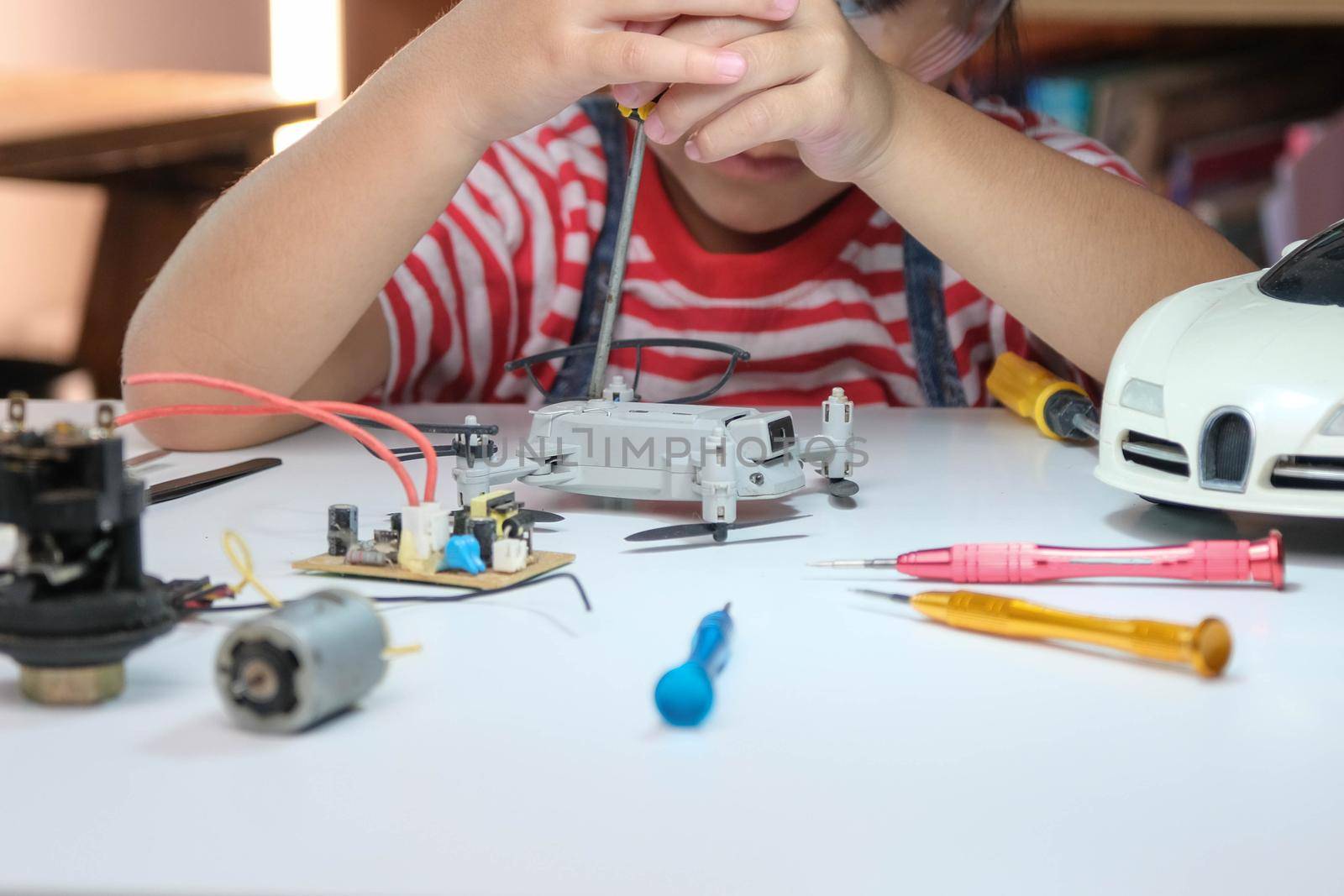 Concentrated little girl repairing her toy drone with a tool in hand and carefully assembles toy drone with screwdriver. STEM Hobbies for advanced smart kids. by TEERASAK