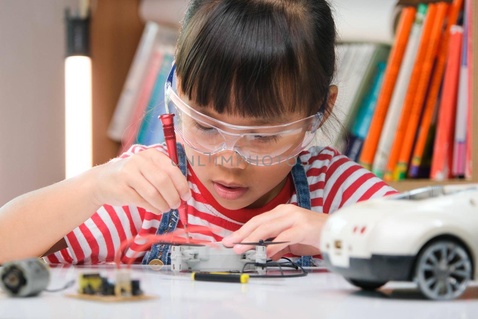 Concentrated little girl repairing her toy car with a tool in hand and carefully assembles toy car with screwdriver. STEM Hobbies for advanced smart kids.