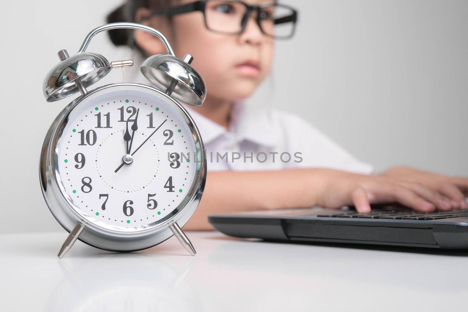 Little businesswoman with laptop working in office with vintage alarm clock on table. Children, Business and Time Concepts.