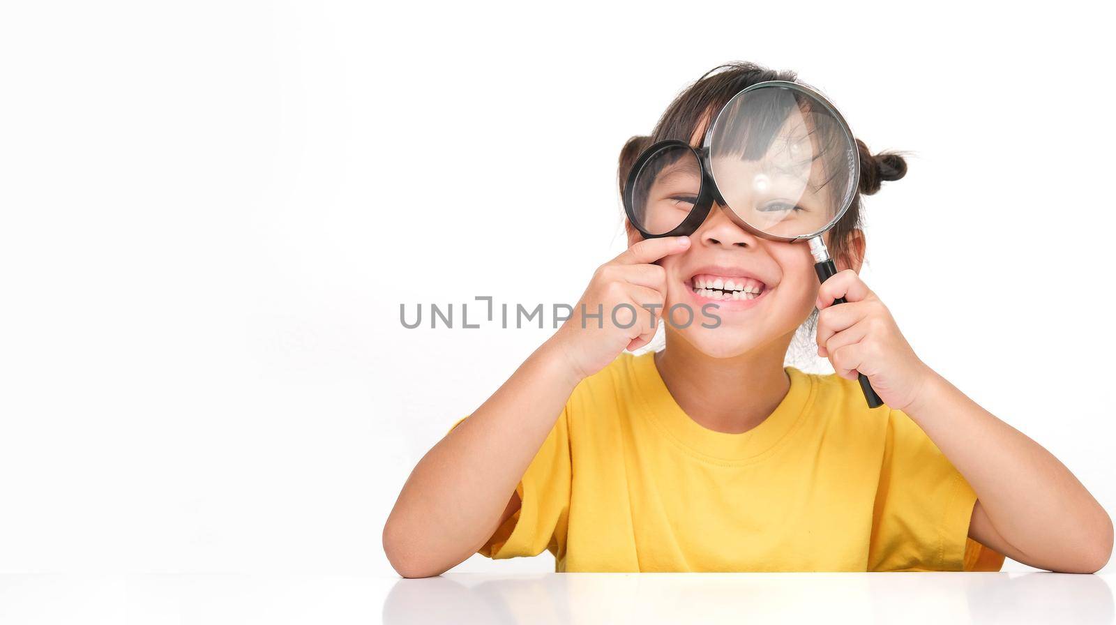 Cute dark haired girl smiling happily holding two magnifying glasses on her eyes isolated on a white background and looking at the camera.