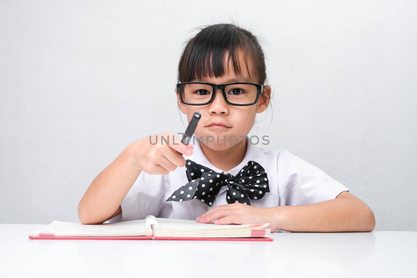 Cute Asian little girl plays teacher role game or little businesswoman taking notes while working in the office. Homeschool children's play and learning. by TEERASAK